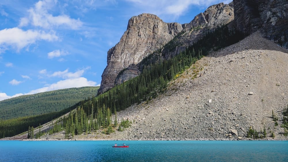 Moraine Lake in Banff National Park, Alberta, Canada, with turquoise water, canoe and Rocky Mountain cliffs Moraine Lake in Banff National Park, Alberta, Canada, with vivid turquoise water, a red canoe crossing the lake and steep forested Rocky Mountain cliffs rising beneath a blue sky.