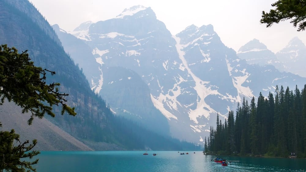 Moraine Lake in Banff National Park, Alberta, Canada with Canoes, Turquoise Water and Mountain Peaks Turquoise Moraine Lake in Banff National Park, Alberta, Canada, with small canoes on the water below snow-streaked mountain peaks and dense evergreen forest.