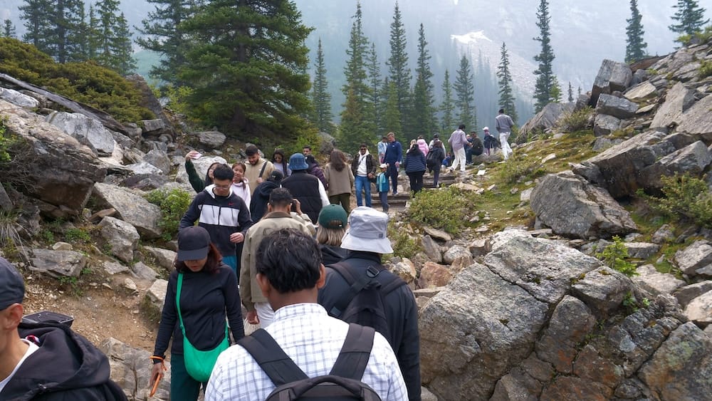 Crowded Rockpile Trail at Moraine Lake, Banff National Park, Alberta, Canada Crowds climbing the rocky Rockpile trail at Moraine Lake in Banff National Park, Alberta, Canada, with large boulders, evergreen trees and mountain slopes surrounding the busy path.