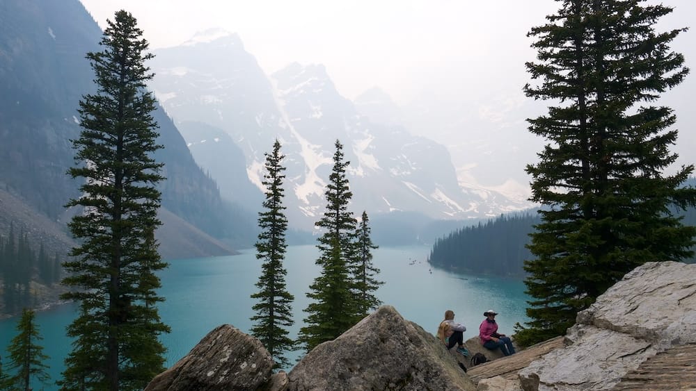 Moraine Lake Rockpile Viewpoint in Banff National Park, Alberta, Canada with Mountain and Lake Views Elevated view of turquoise Moraine Lake from the Rockpile viewpoint in Banff National Park, Alberta, Canada, framed by evergreen trees, rocky foreground and hazy mountain peaks.