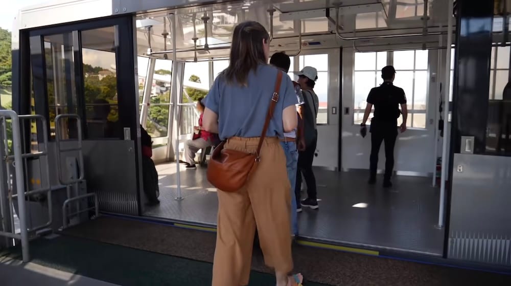 Audrey Bergner boarding a Mt. Hakodate Ropeway gondola in Hakodate, Hokkaido, Japan, with other passengers already inside the cable car and the station platform visible around the entrance.