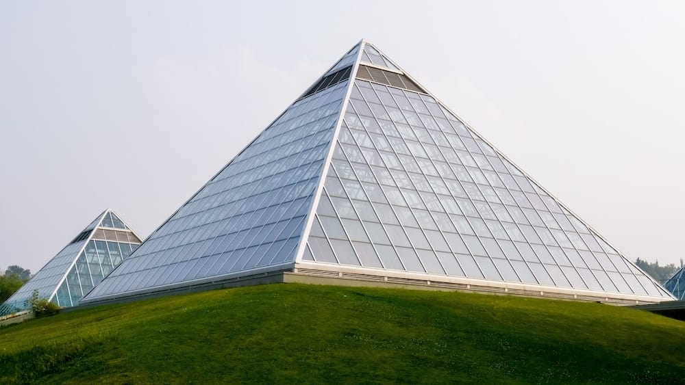 Muttart Conservatory glass pyramids, exterior view, Edmonton, Alberta, Canada. Exterior view of two of the Muttart Conservatory's glass pyramids rising above a grass embankment in Edmonton, Alberta, Canada, against a hazy sky.