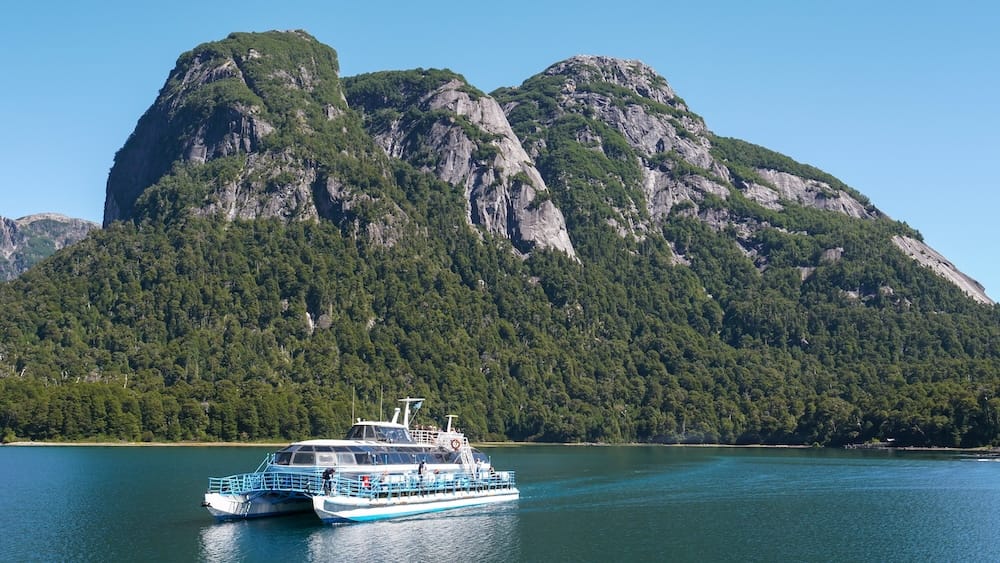 Tourist catamaran crossing Nahuel Huapi Lake near Bariloche, Patagonia, Argentina A tourist catamaran crosses the blue waters of Nahuel Huapi Lake near Bariloche, Río Negro, Patagonia, Argentina, beneath steep forested mountains and exposed rocky cliffs under a clear sky.