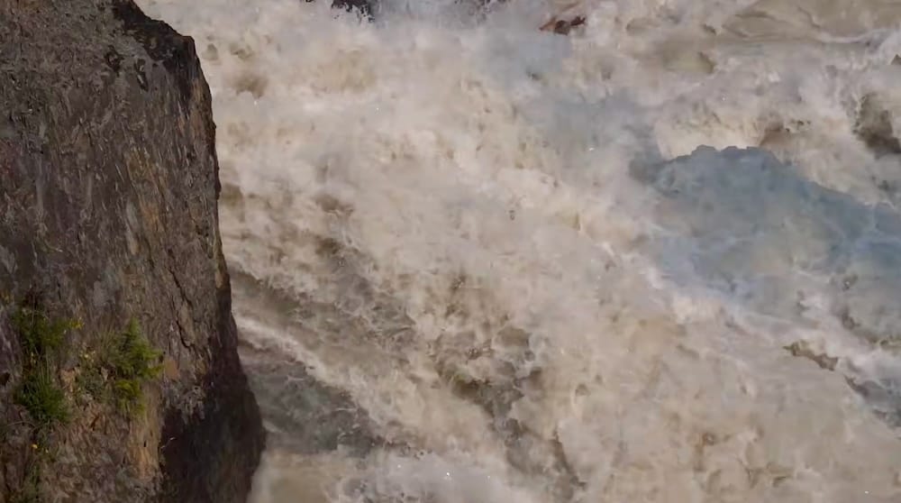 Close-up of turbulent whitewater from the Kicking Horse River crashing beside dark exposed rock at Natural Bridge in Yoho National Park, British Columbia, Canada.