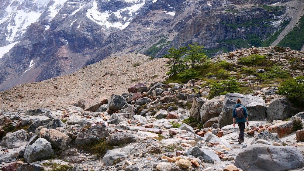 Rocky terrain near Mirador Maestri on the Laguna Torre hike in El Chaltén, Argentina, showing a lone hiker navigating a rugged moraine landscape beneath steep Patagonian cliffs, illustrating the wild scenery beyond the main viewpoint.
