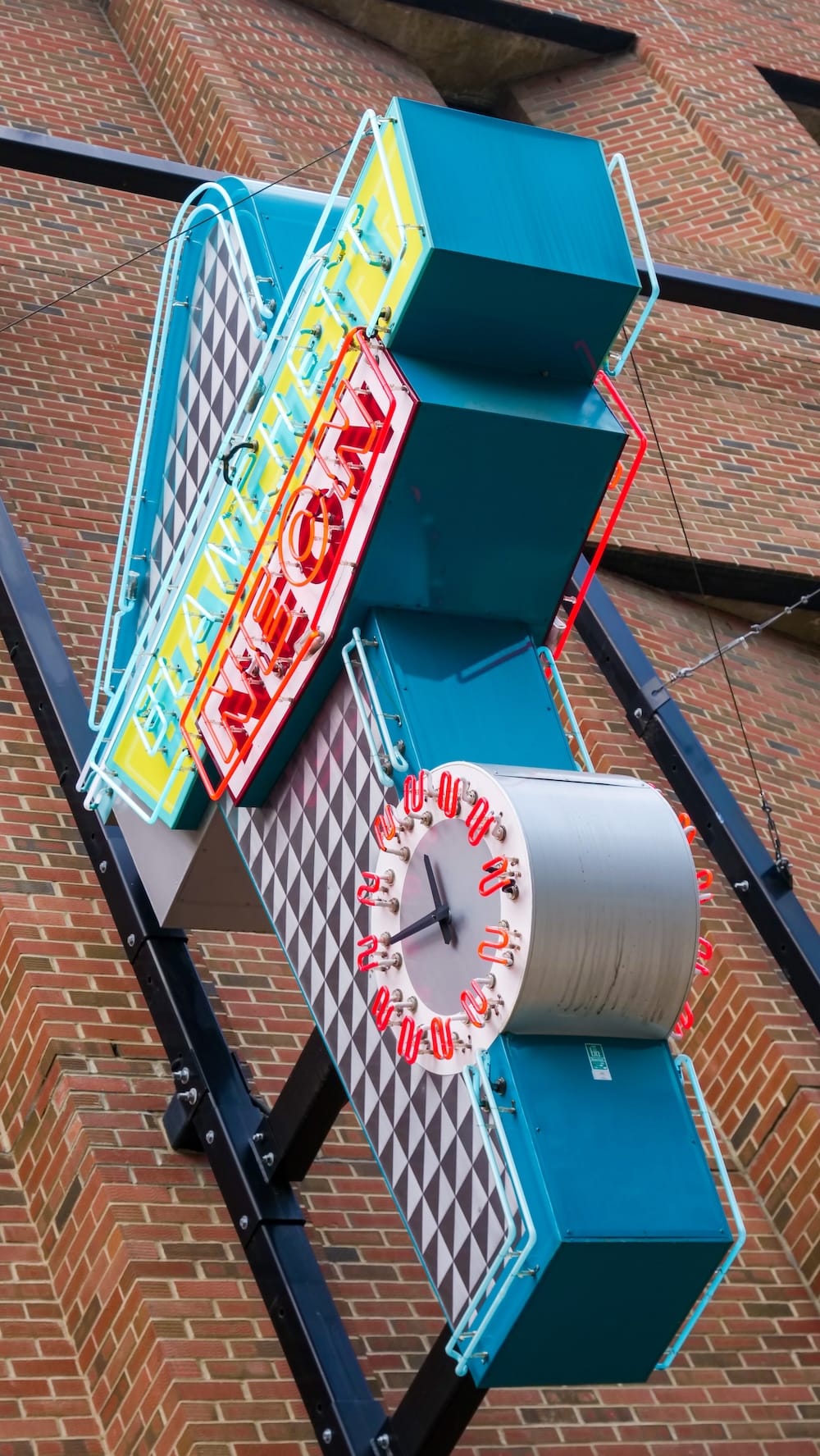 Cartel y reloj de Blanchett Neon en el Neon Sign Museum, 104 Street, Edmonton, Alberta, Canadá Cartel de "Blanchett Neon" en verde azulado y amarillo, con un reloj redondo de neón incorporado, montado en una pared de ladrillo del Neon Sign Museum en la 104 Street, en el centro de Edmonton, Alberta, Canadá, fotografiado en ángulo desde abajo.