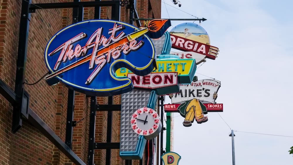Restored storefront signs at Edmonton’s Neon Sign Museum in Alberta, Canada Close-up of restored vintage neon signs mounted along a brick wall at Edmonton’s Neon Sign Museum in Alberta, Canada, including colourful storefront lettering, clocks and illustrated business signs.