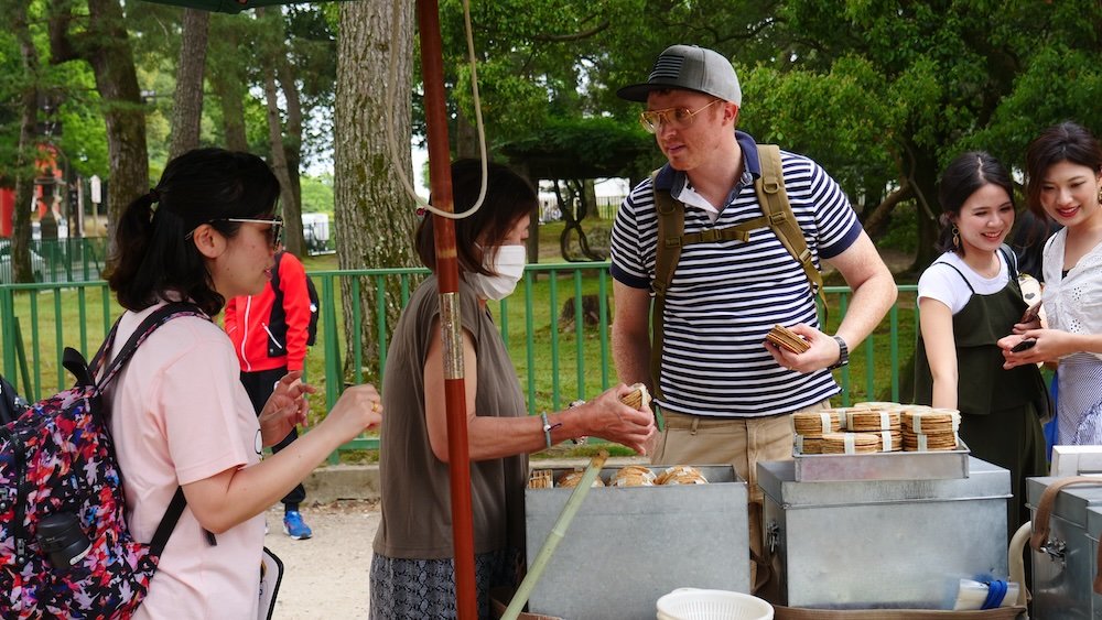 Nomadic Samuel buying snacks to feed the deer in Nara, Japan 