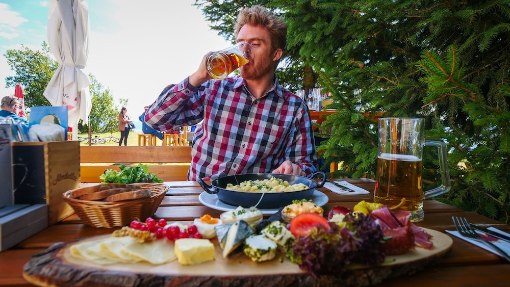 Nomadic Samuel chugging beer and feasting on a Gaisberg hike in Austria 