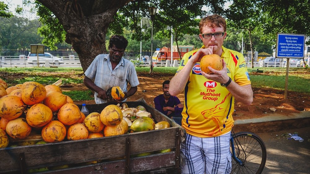 Nomadic Samuel drinking a coconut in India 