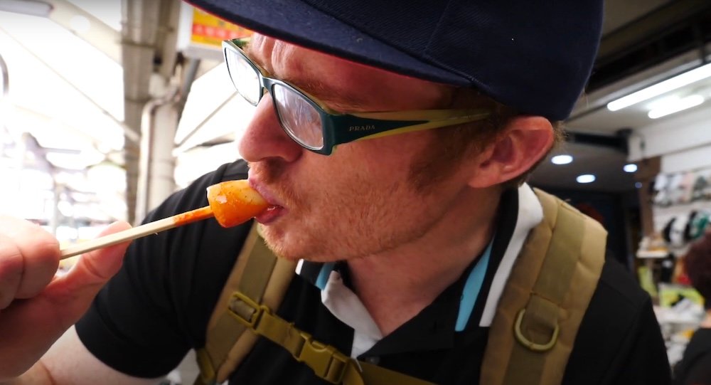 Nomadic Samuel eating a spicy Korean rice cake at Seomun market in Daegu, South Korea 