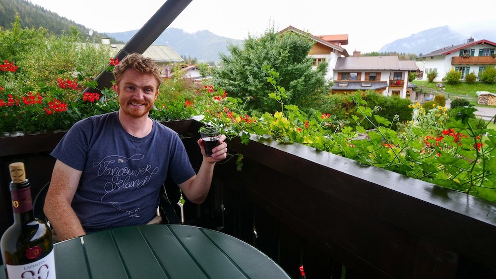 Nomadic Samuel enjoying a glass of wine with great views from our guesthouse accommodations whilst visiting Berchtesgaden, Germany