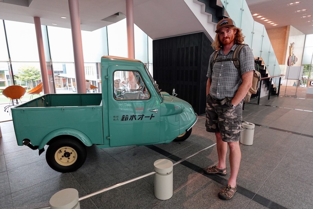 Nomadic Samuel enjoying visiting Matsumoto, Japan standing beside a miniature truck 