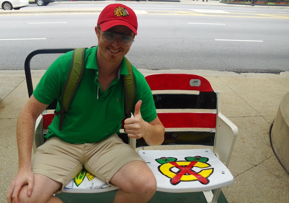 Nomadic Samuel enthusiastically sitting down on a Chicago Blackhawks chair along the Magnificent Mile