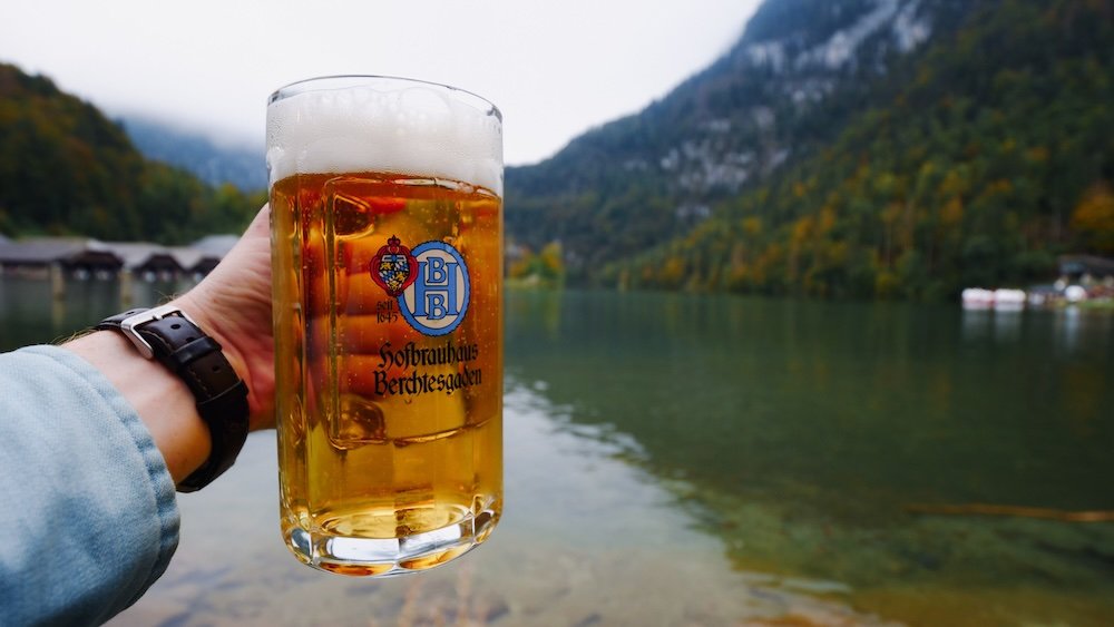 Nomadic Samuel holding a pint of German beer from Hofbrauhaus overlooking the pristine lake in Berchtesgaden, Germany 