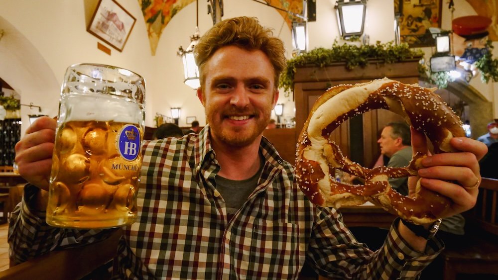 Nomadic Samuel holding a huge pint of beer and giant pretzel in Munich, Germany 