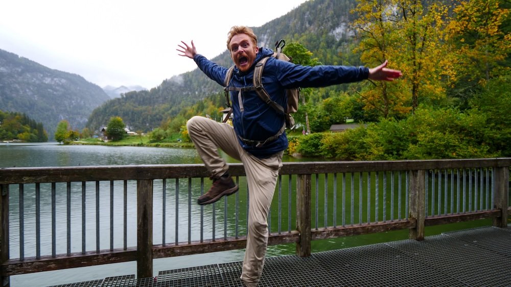 Nomadic Samuel thrilled to be visiting Berchtesgaden jumping up in the air with lake scenery in the background