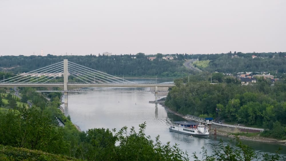 Elevated view over the North Saskatchewan River Valley in Edmonton, Alberta, Canada, with a cable-stayed bridge, riverboat, wooded banks and city roads crossing the green corridor.
