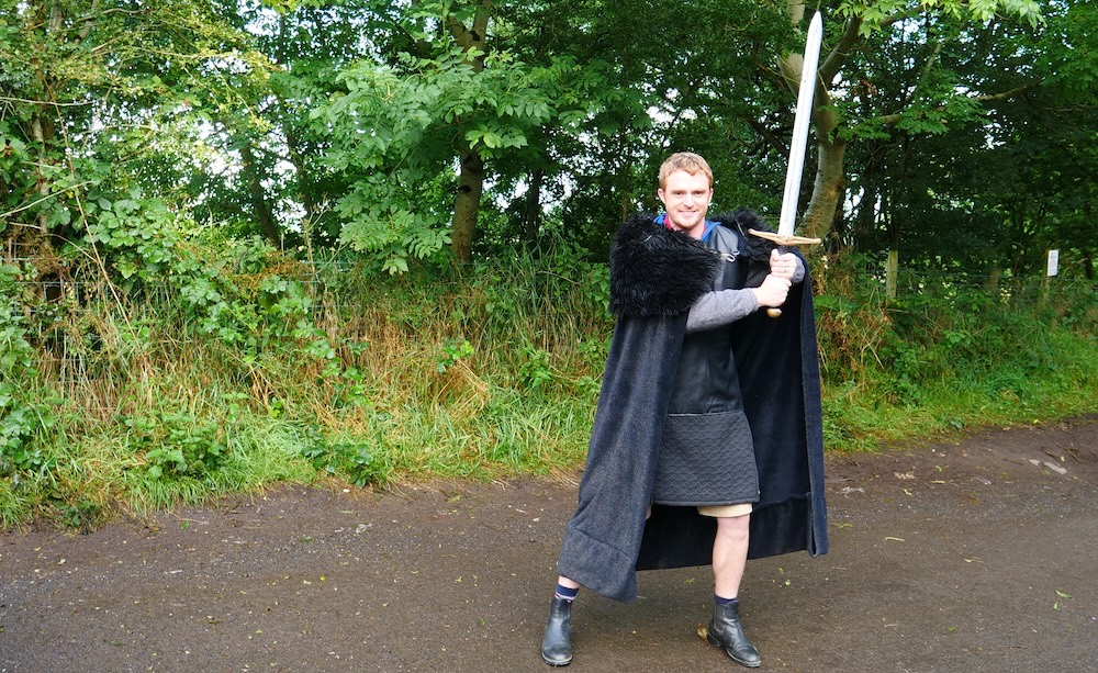 Northern Ireland — Nomadic Samuel poses with a sword in full Game of Thrones-style costume during a filming experience for the award-winning 24 Hours in the UK travel campaign by iAmbassador, capturing a playful storytelling moment.