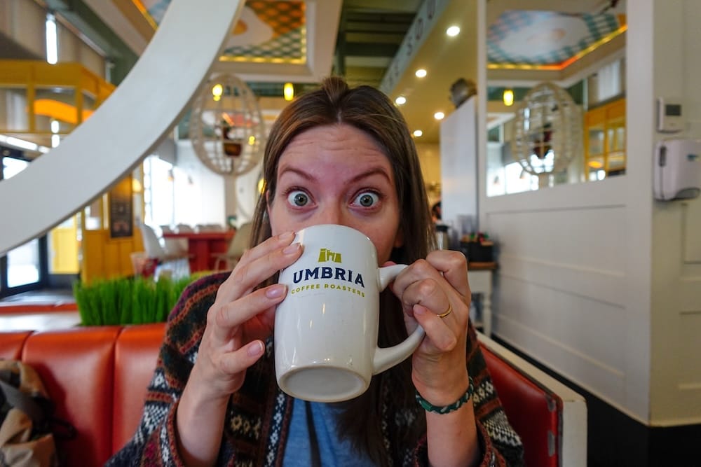 Audrey Bergner mira con los ojos muy abiertos por encima del borde de una taza de Umbria Coffee Roasters sentada en un box de OEB Breakfast Co. en el centro de Edmonton, Alberta, Canadá.