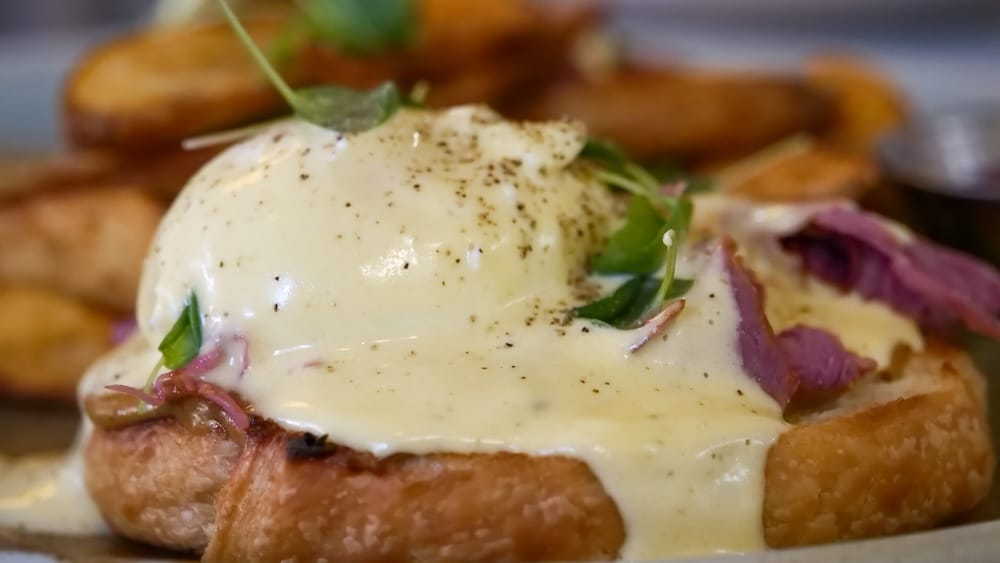 Foto macro de un huevo poché cubierto de salsa holandesa sobre carne ahumada estilo Montreal y un pan brioche tostado, parte de un Benny en OEB Breakfast Co. en el centro de Edmonton.