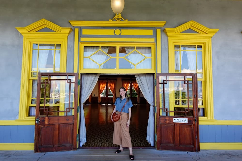 Audrey Bergner stands in the open doorway of the Old Public Hall of Hakodate Ward in Hakodate, Hokkaido, Japan, framed by bright yellow trim, wooden doors and the elegant interior of the historic building.