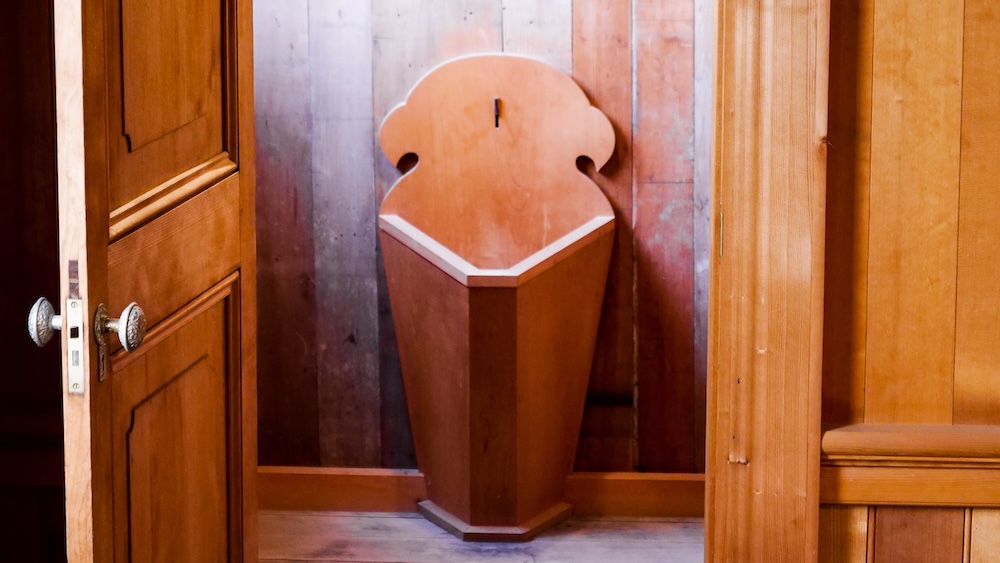 Open panelled wooden door with an ornate metal doorknob revealing a carved wooden standing bathroom fixture against vertical timber wall planks inside the Old Public Hall of Hakodate Ward in Hakodate, Hokkaido, Japan.