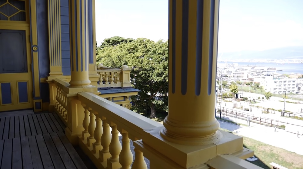 Old Public Hall of Hakodate Ward Balcony in Motomachi, Hokkaido, Japan, with Yellow Columns and Harbour Views View from the balcony of the Old Public Hall of Hakodate Ward in Motomachi, Hokkaido, Japan, showing yellow columns, decorative balustrades, wooden flooring and the city rooftops and harbour beyond.