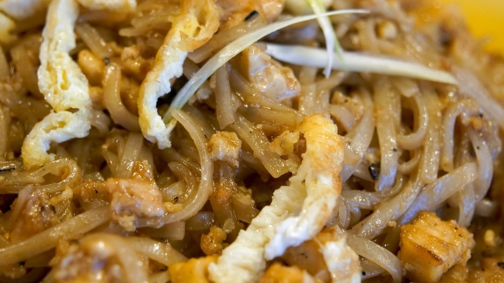 Close-up macro details of Pad Thai from Family Thai Restaurant in Cranbrook, British Columbia, highlighting glossy rice noodles, egg, chicken, crushed peanuts, and sauce-coated textures that showcase the richness and authenticity of this classic Thai comfort-food dish.