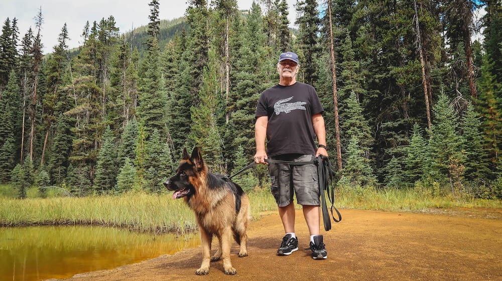 Daniel Bergner and Togo at the Paint Pots in Kootenay National Park, British Columbia, Canada Daniel Bergner stands with Togo beside an ochre-coloured mineral pool at the Paint Pots in Kootenay National Park, British Columbia, Canada, with dense evergreen forest filling the background.
