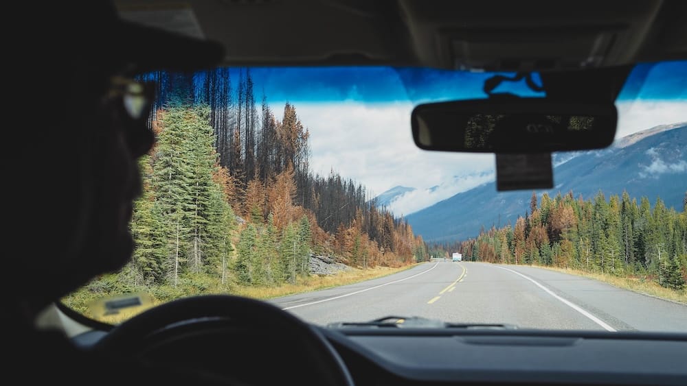 Scenic drive toward the Paint Pots in Kootenay National Park, British Columbia, Canada, with mountain views View through a vehicle windshield while driving toward the Paint Pots in Kootenay National Park, British Columbia, Canada, with a two-lane highway, evergreen forest and cloud-covered mountain slopes ahead.