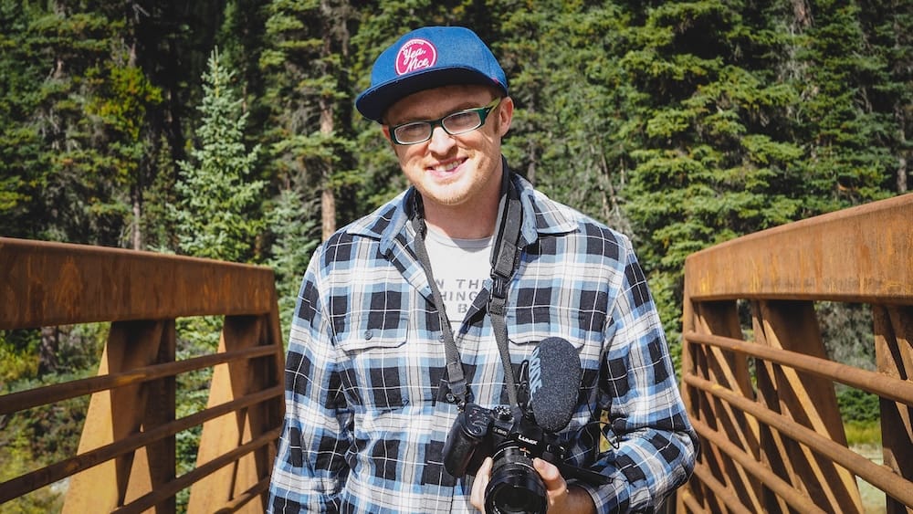 Samuel Jeffery with camera on the Paint Pots Trail bridge in Kootenay National Park, British Columbia, Canada Samuel Jeffery stands on the rust-coloured pedestrian bridge on the Paint Pots Trail in Kootenay National Park, British Columbia, Canada, holding a camera with evergreen forest and the trail area behind him.