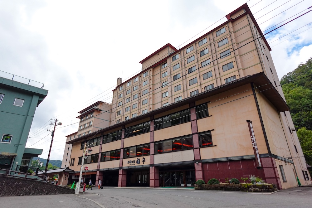 Exterior of Park Hotel Miyabitei, the ten-storey resort hotel where we stayed in Noboribetsu Onsen, Hokkaido, Japan The multi-storey beige facade of Park Hotel Miyabitei rises above the street, with its name sign over the entrance and a forested hillside beside it in Noboribetsu Onsen, Hokkaido, Japan.