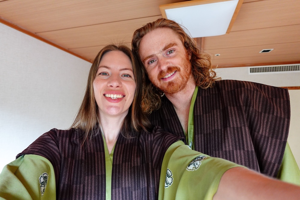 Yukata selfie at Park Hotel Miyabitei, Noboribetsu Onsen, Hokkaido, Japan – Samuel Jeffery and Audrey Bergner Audrey Bergner and Samuel Jeffery smile in a selfie, wearing matching green yukata with dark striped vests, inside their room at Park Hotel Miyabitei in Noboribetsu Onsen, Hokkaido, Japan.
