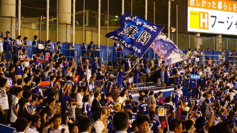 Passionate Chunichi Dragons supporters wave large blue flags and cheer together from the visiting outfield section during an NPB baseball game at Meiji Jingu Stadium in Tokyo, Japan.
