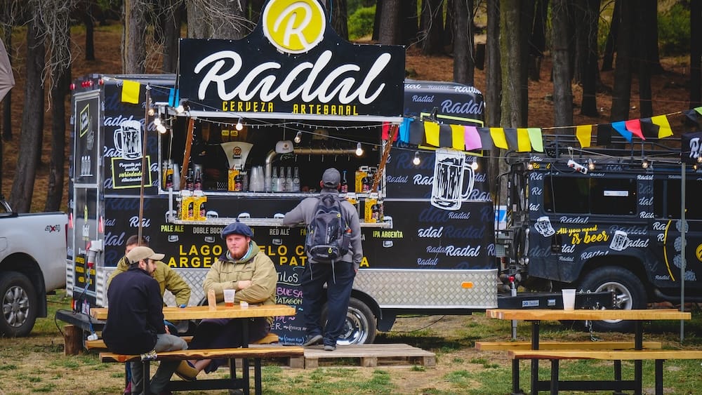 Artisanal beer truck serving local craft brews at Fiesta Nacional del Asado in Radal, Patagonia, Argentina, surrounded by pine forest, highlighting the casual outdoor beer culture where fresh pours are enjoyed alongside festivals, food, and open-air gatherings.
