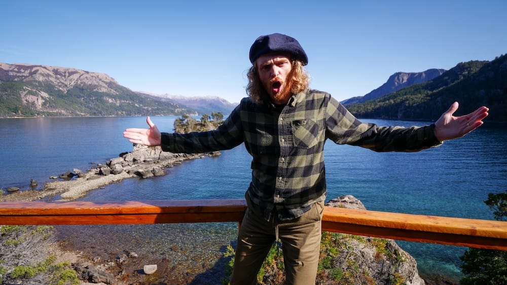 Samuel Jeffery reacting to rare calm conditions at Estancia Arroyo Verde in Patagonia, arms wide over lake and mountain views, capturing a fleeting break in the relentless Roaring 40s winds that normally dominate this exposed region