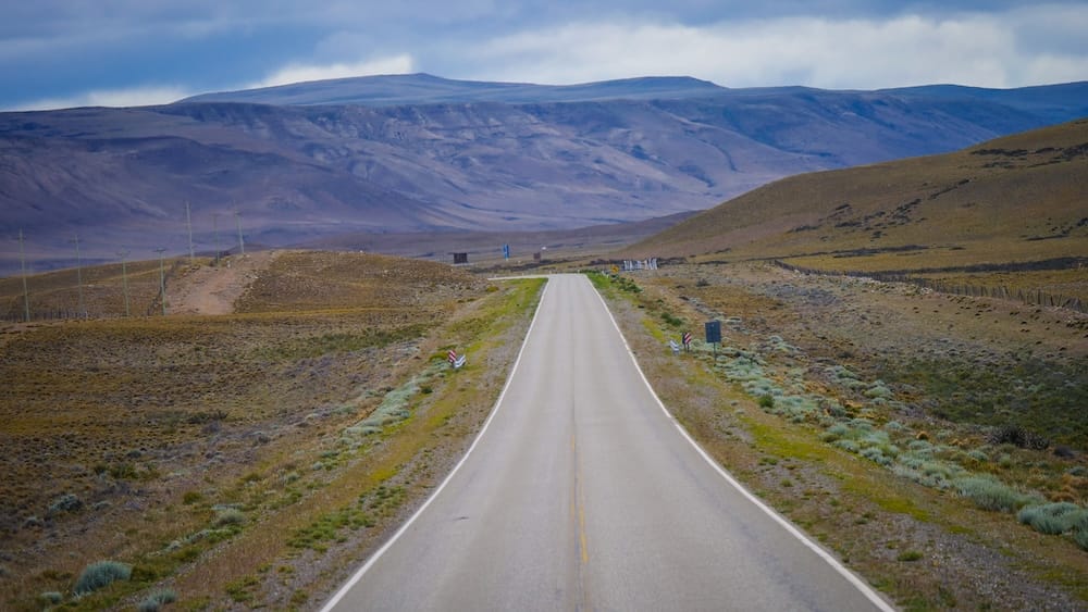 Patagonia road to El Calafate across open steppe landscape in Argentina Long empty road leading toward El Calafate Patagonia Argentina cutting through vast steppe landscape with rolling hills and distant mountains, emphasizing isolation and travel distances
