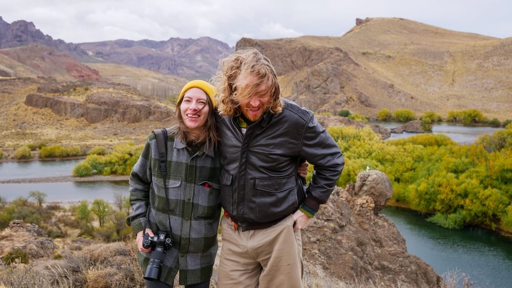 Patagonian wind blasting Samuel Jeffery and Audrey Bergner near Estancia Arroyo Verde as they lean together against powerful gusts, hair whipped sideways, capturing the physical force of Patagonia’s relentless Roaring 40s winds