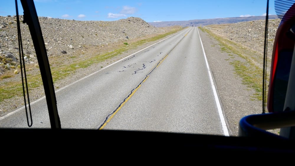 Patagonian Highway Near El Calafate, Santa Cruz, Argentina, Seen from a Long-Distance Bus An empty Patagonian highway stretches toward the horizon near El Calafate in Santa Cruz, Argentina, viewed through the front window of a long-distance bus crossing the region’s open, rocky landscape.