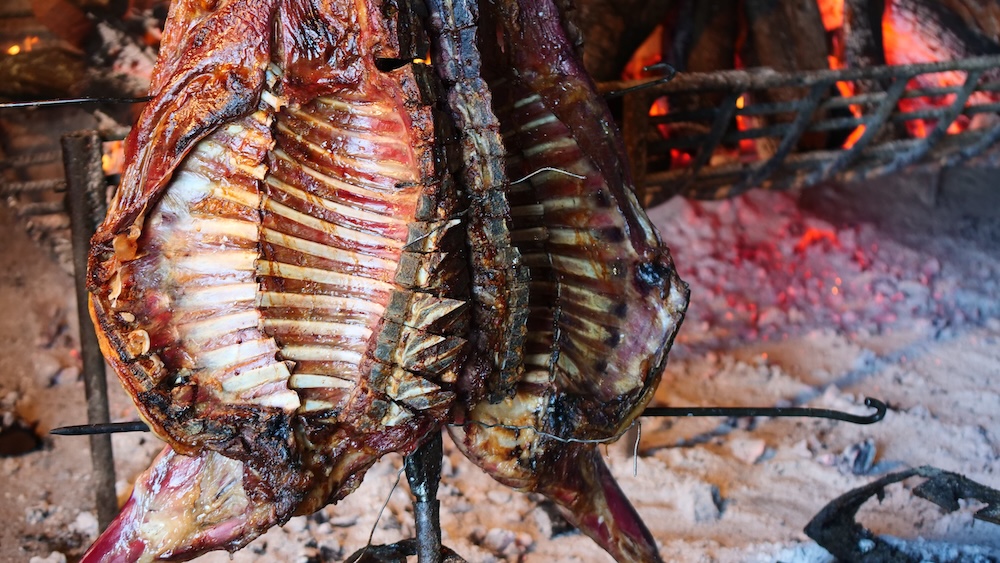 Patagonian lamb roasting over open fire at an estancia in El Chaltén, Patagonia, Argentina, with sizzling meat over glowing embers creating a traditional asado feast and cultural food experience in Los Glaciares region.