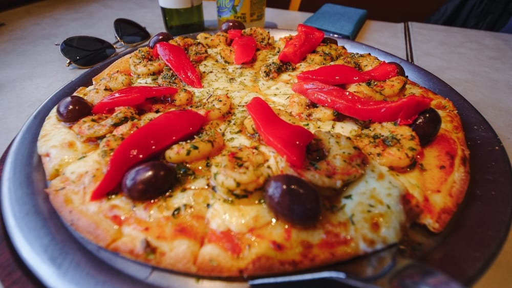 Shrimp and roasted red pepper pizza in Comodoro Rivadavia Patagonia with olives garlic and herbs on coastal style crust Shrimp and roasted red pepper pizza in Comodoro Rivadavia Chubut Argentina topped with mozzarella, olives, garlic, herbs, and oil-coated shrimp on a golden crust served in a casual Patagonian coastal restaurant.