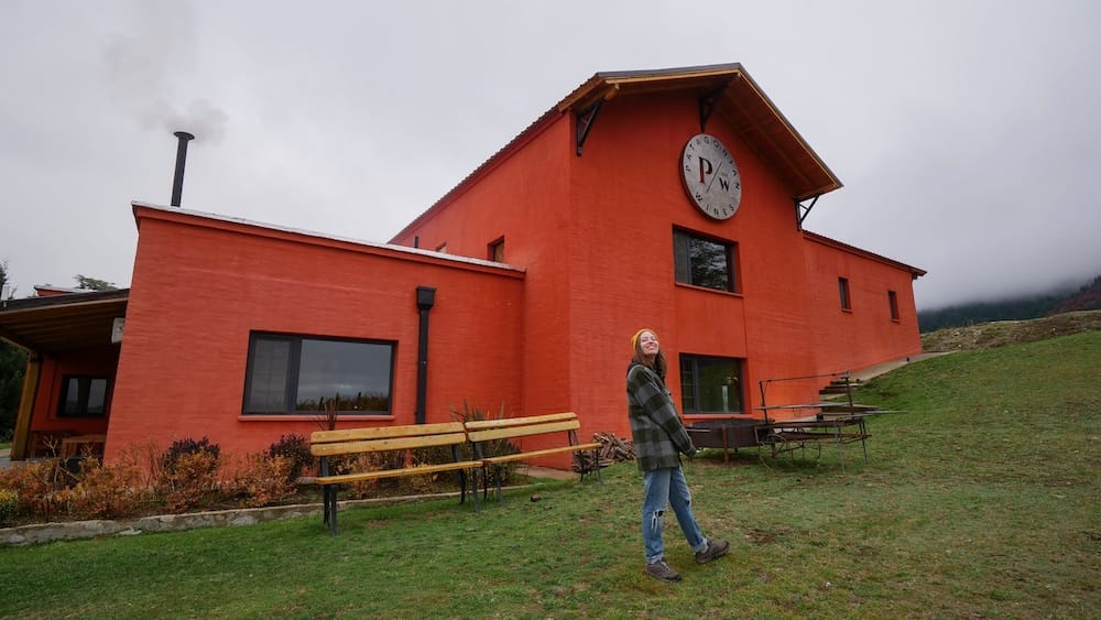 Audrey Bergner outside the Patagonian Wines building in El Hoyo, Chubut, Patagonia, Argentina Audrey Bergner stands outside the bright red Patagonian Wines building in El Hoyo, Chubut, Patagonia, Argentina, with the winery logo visible on the facade and low cloud hanging over the surrounding hillside.