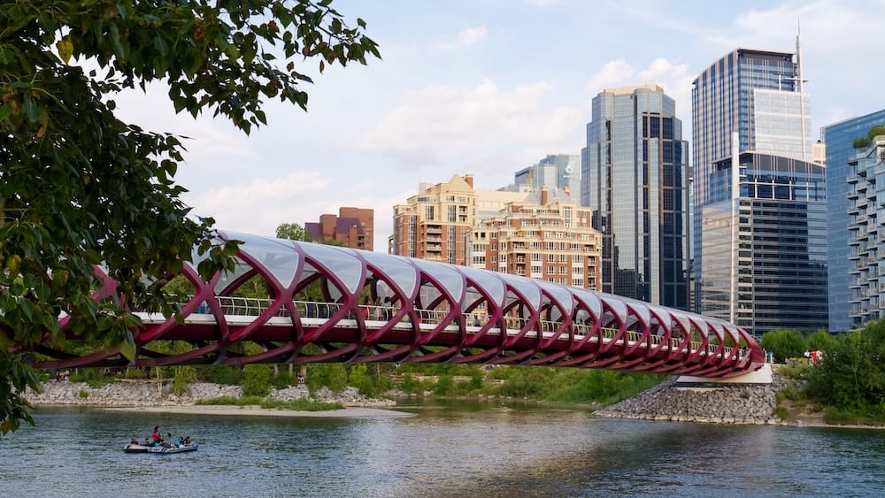 Peace Bridge and downtown skyline over the Bow River, Calgary, Alberta, Canada The red Peace Bridge crossing the Bow River with people rafting below and Calgary's downtown skyline of glass towers rising behind it, Calgary, Alberta, Canada.