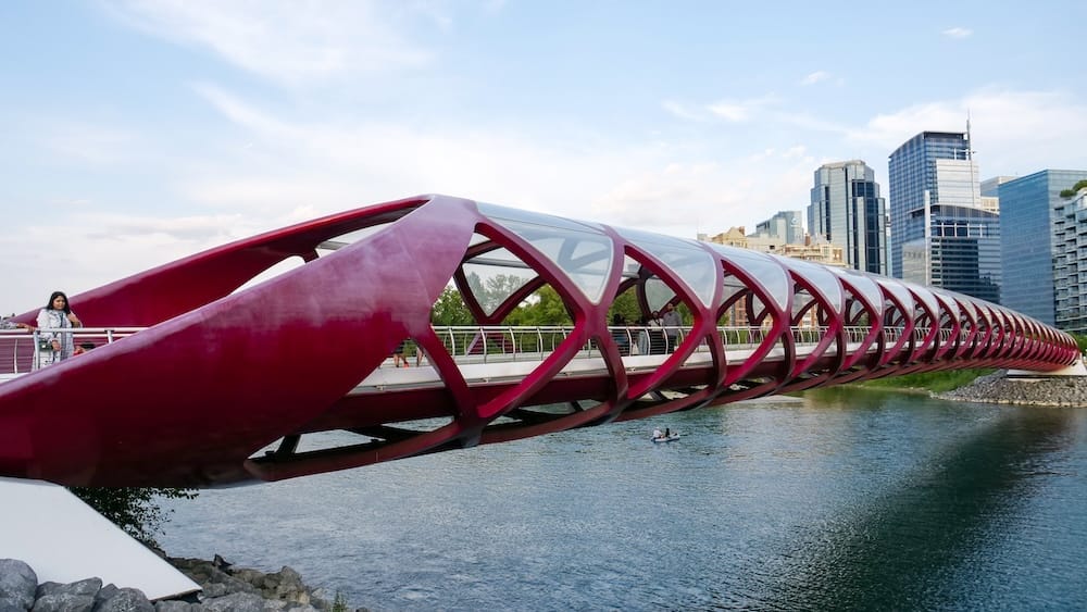 Peace Bridge crossing the Bow River with downtown Calgary skyline in Alberta, Canada Calgary’s red Peace Bridge crosses the Bow River in Calgary, Alberta, Canada, with pedestrians on the bridge, green riverbanks and downtown high-rises rising in the background.