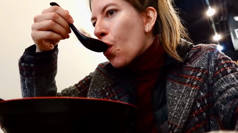 Audrey Bergner drinks pho broth from a spoon over a red bowl at Peak Cafe in Banff, Alberta, Canada.