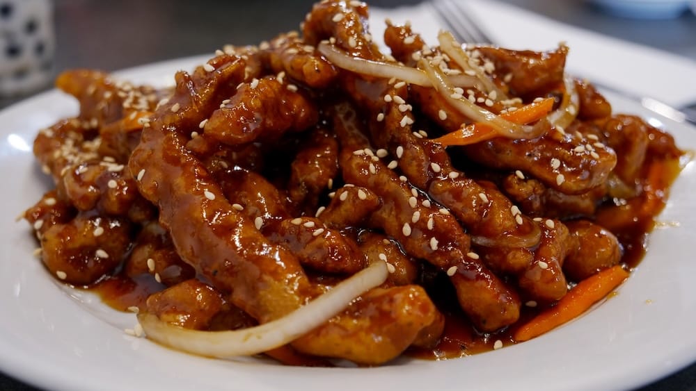 Ginger Beef at Peak Cafe in Banff, Alberta, Canada, with Crispy Glazed Beef and Sesame Seeds Close-up of ginger beef served at Peak Cafe in Banff, Alberta, Canada, with crispy glazed beef strips, sliced onion, carrot and sesame seeds piled on a white plate.