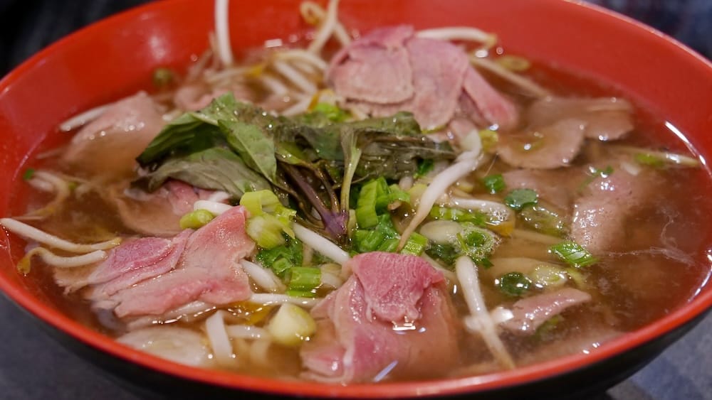 Pho de carne con fideos, hierbas y brotes de soja en Peak Cafe, Banff, Alberta, Canadá Primer plano de pho de carne en Peak Cafe, Banff, Alberta, Canadá, servido en un bol rojo con finas láminas de carne, fideos de arroz, brotes de soja, cebolla de verdeo y hierbas frescas en caldo caliente.
