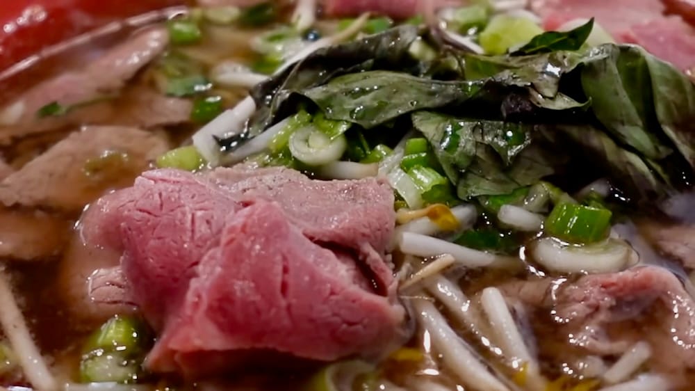 Close-up of rare beef slices, Thai basil, bean sprouts, and green onion in beef pho broth at Peak Cafe in Banff, Alberta, Canada.