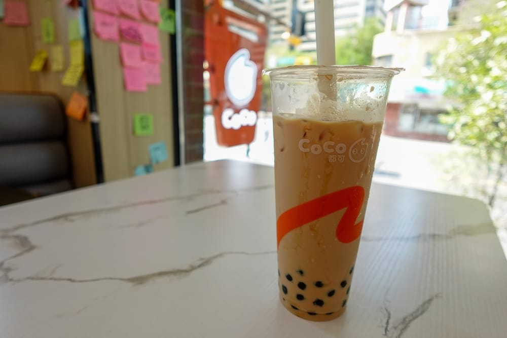 A CoCo Fresh Tea & Juice pearl milk tea with tapioca settled at the bottom, sitting on a marble table near the shop's storefront window in Chinatown, Calgary, Alberta, Canada.